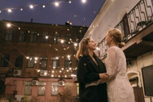 Woman in Black Coat Standing Beside Woman in White Floral Lace Long Sleeve Dress